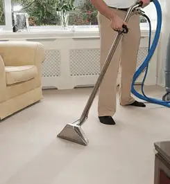 Professional carpet cleaner using a hot-water extraction wand and hose machine in a living room in Cambridge, MA.