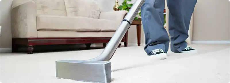 Carpet cleaning technician using a hot-water extraction wand on a light-colored carpet in a living room, Cambridge, MA.